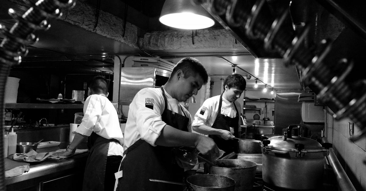 Black and white image of chefs preparing meals in an industrial restaurant kitchen.